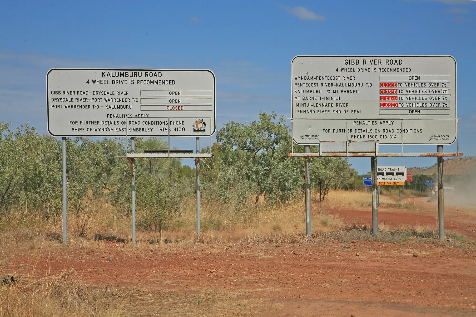 Road-condition signs for the Gibb River Road and Kalumburu Road beside a red dirt road
