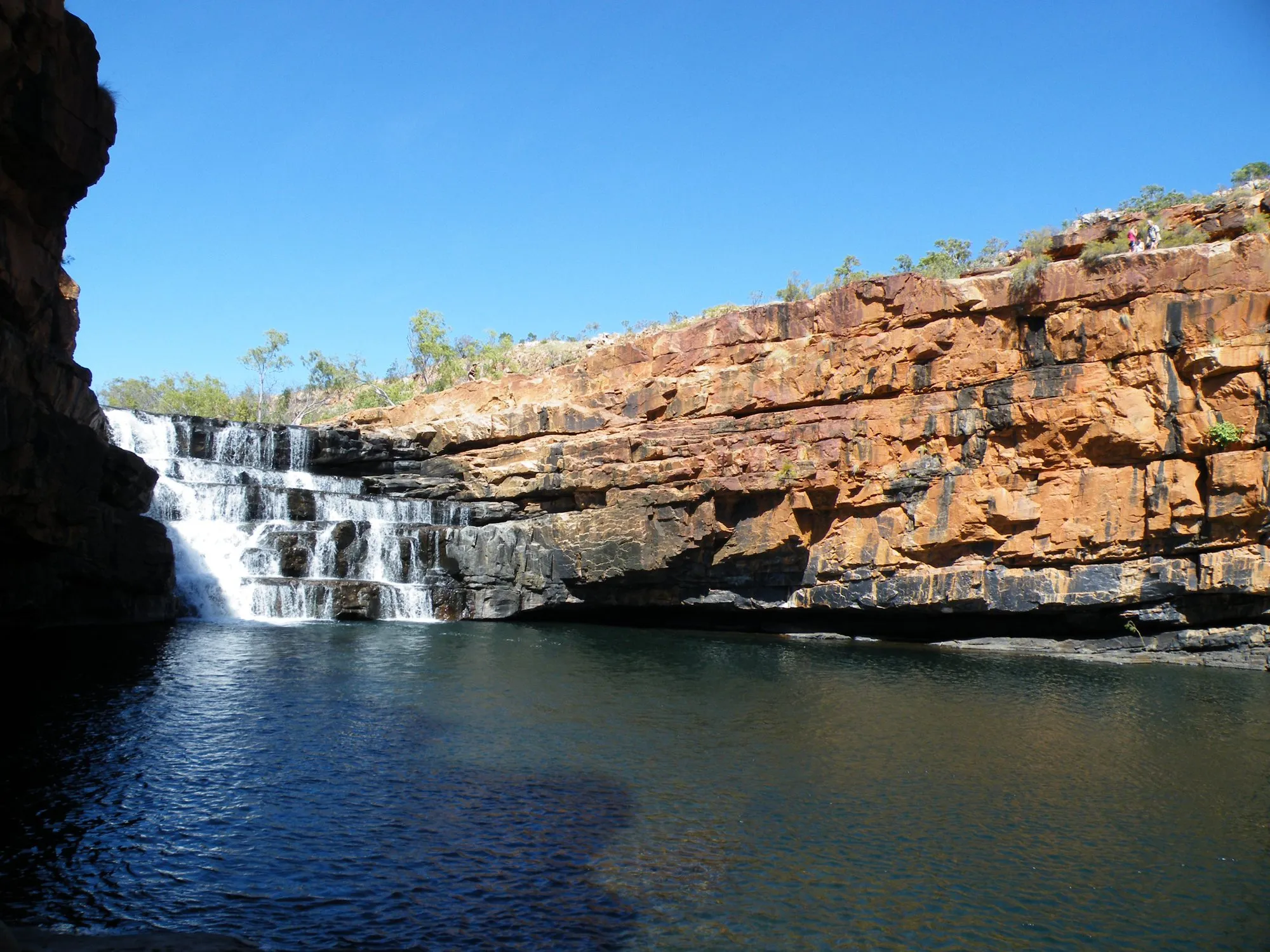 A waterfall spilling over red rock into a dark pool at Bell Gorge