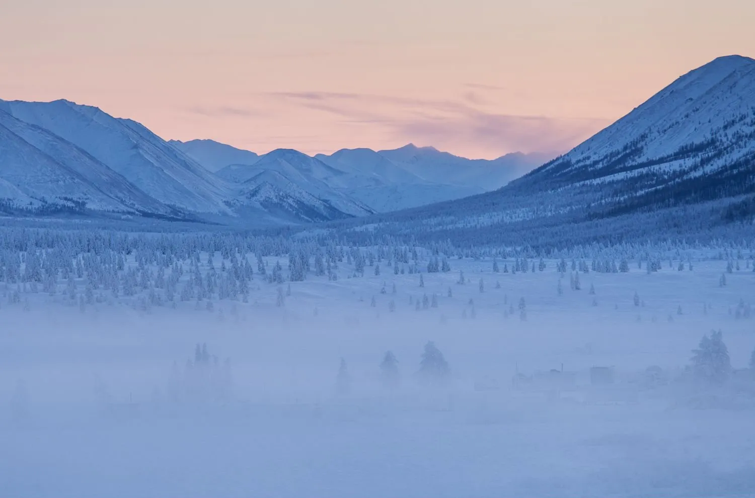 Frozen valley and mountains near Oymyakon after sunset, with ice fog over the forest