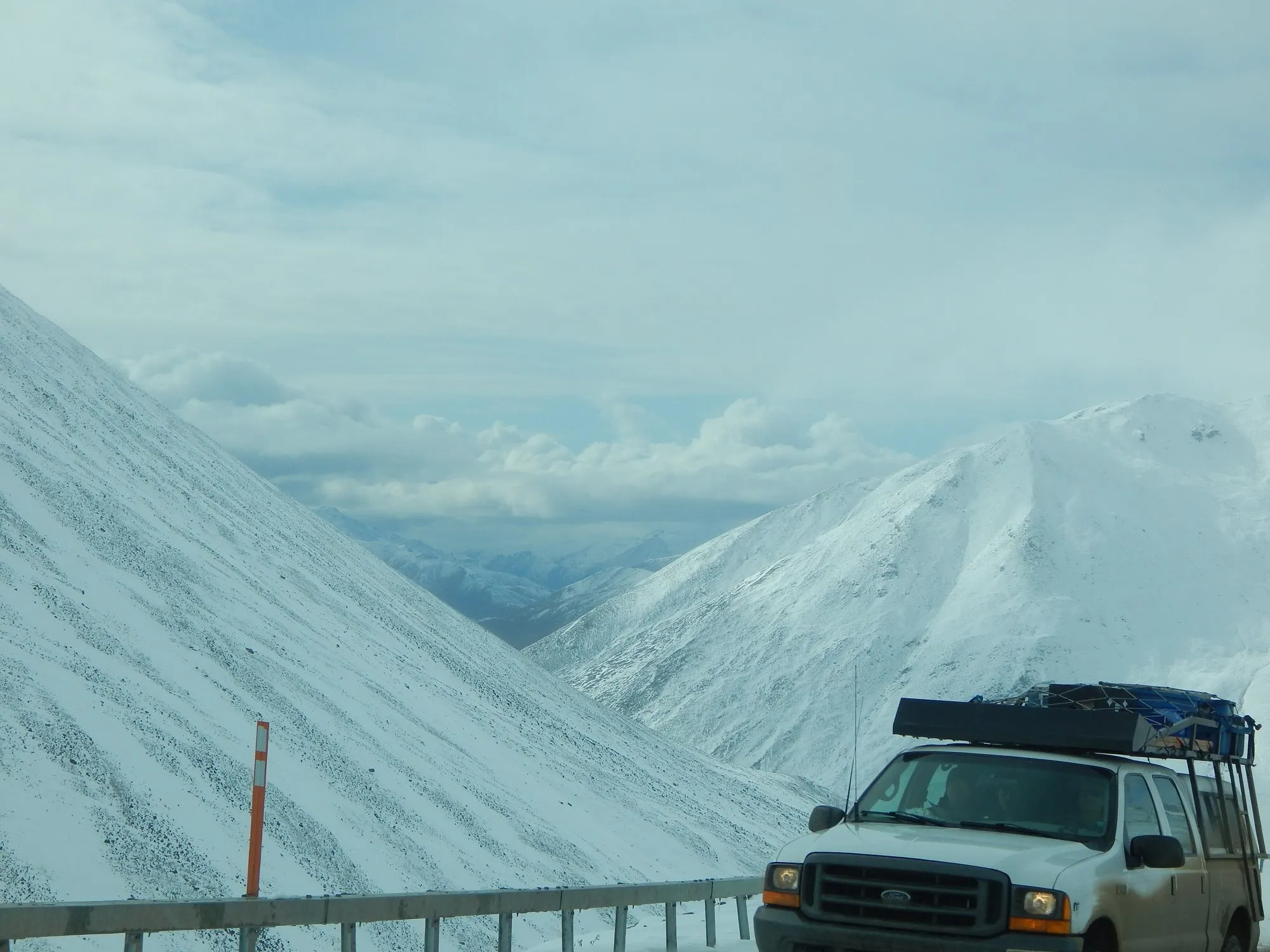 A pickup truck with a roof rack on a snowy road near Atigun Pass