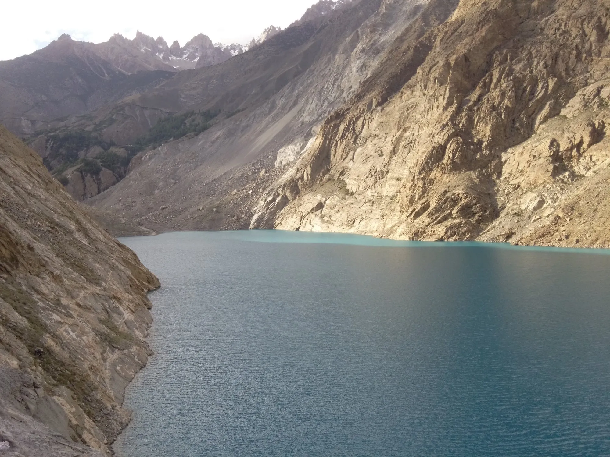 The turquoise Attabad Lake between steep brown mountain walls, seen from the Karakoram Highway