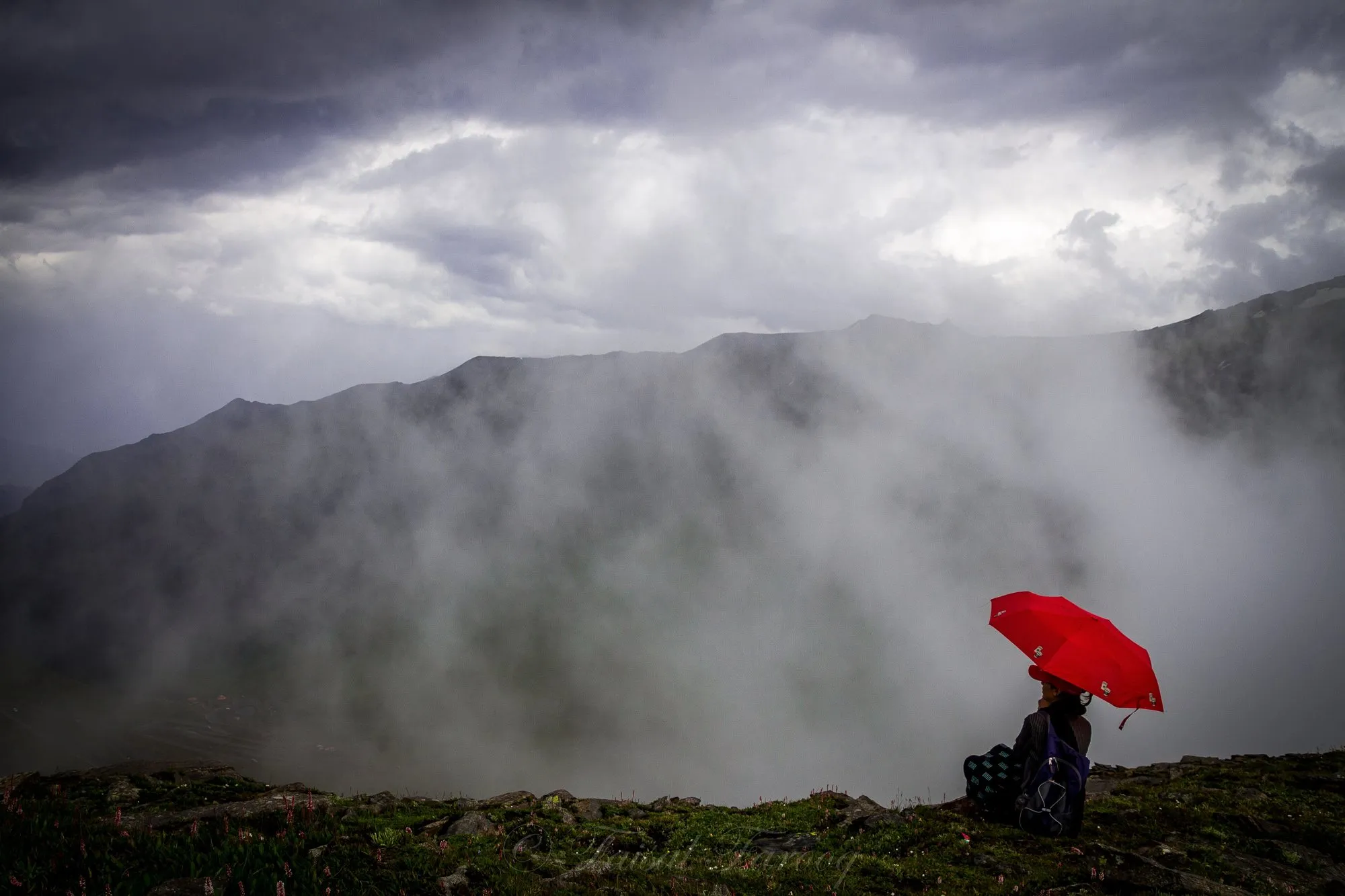 A person under a red umbrella on a misty hillside at the Babusar Pass