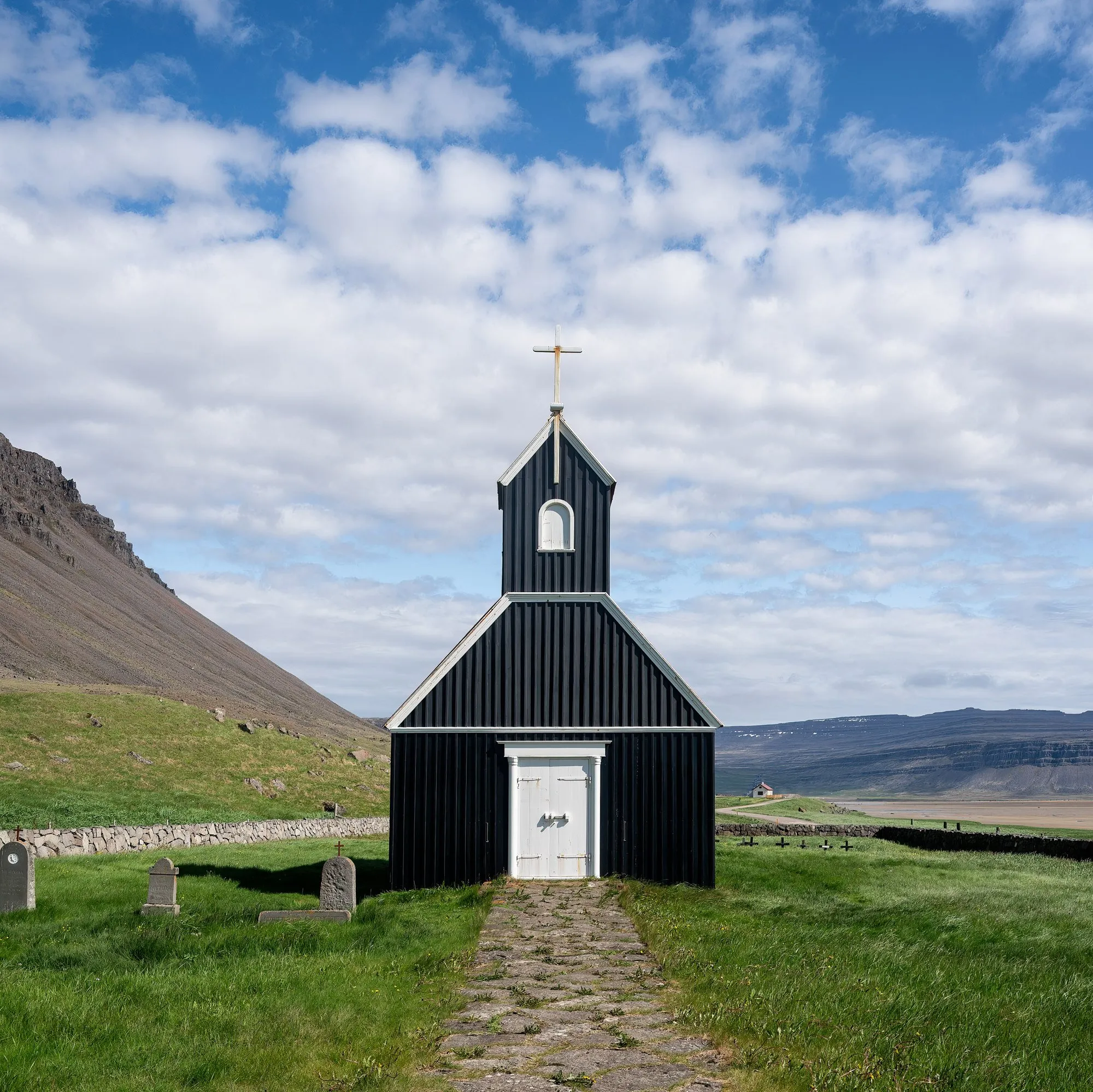 A small black wooden church with a white door on green grass at Rauðisandur