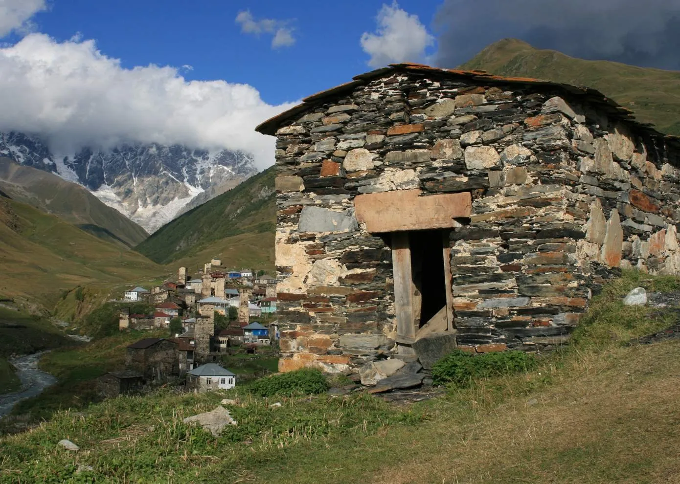 A small stone church in Chazhashi with the village and Shkhara behind