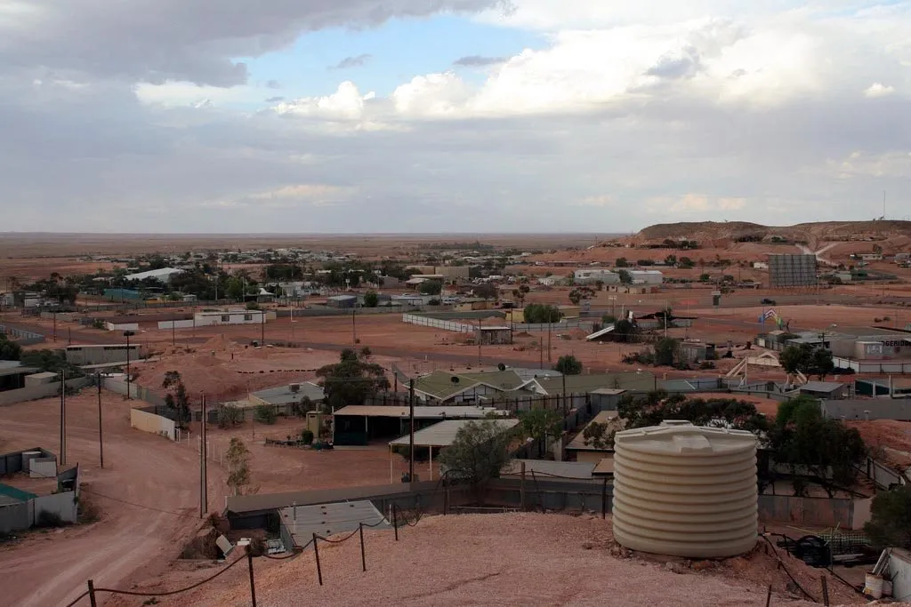 Coober Pedy's low buildings and water tanks spread across a flat red landscape