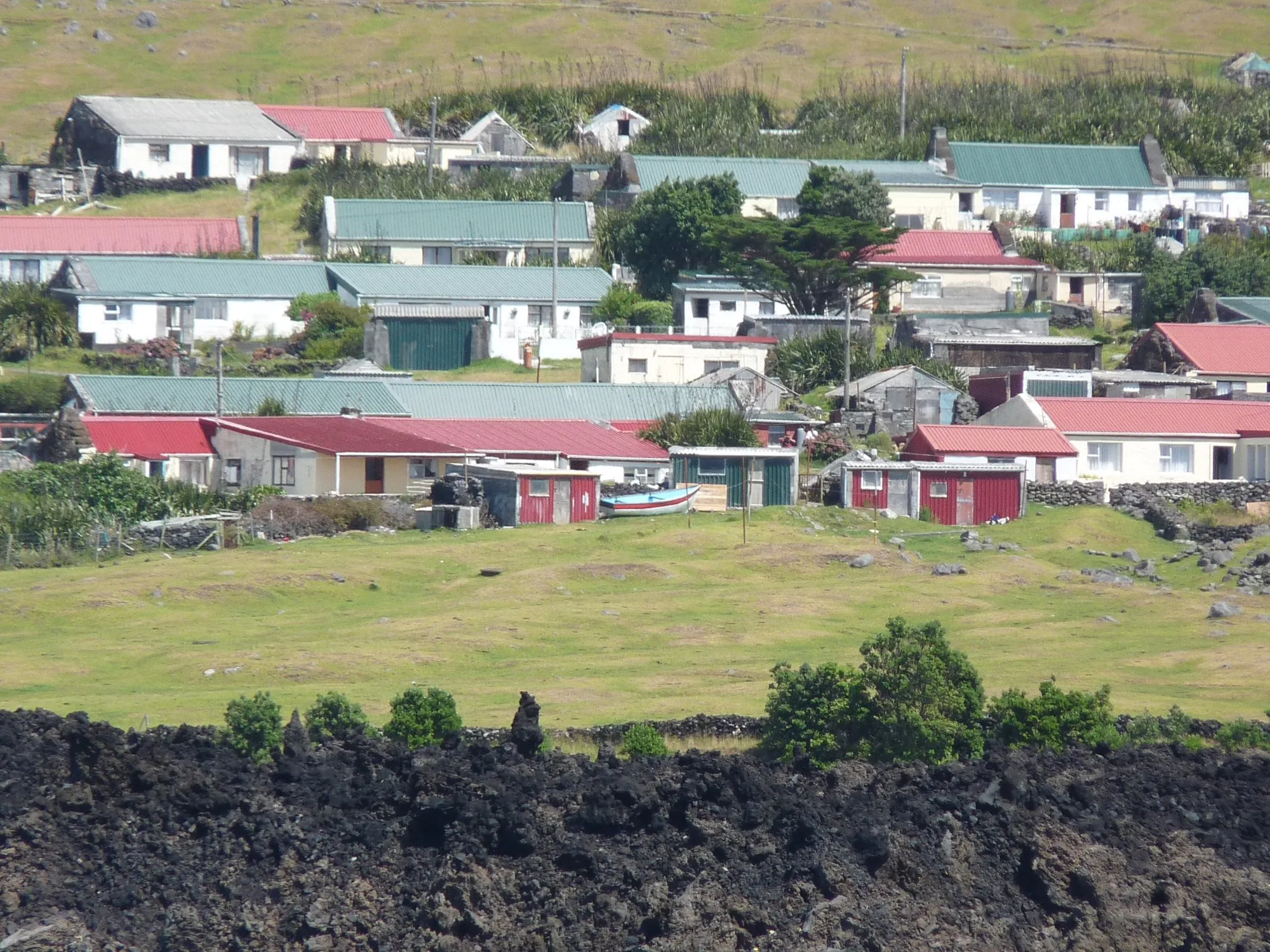 Houses with red and green roofs on grassland above black lava rock in Edinburgh of the Seven Seas