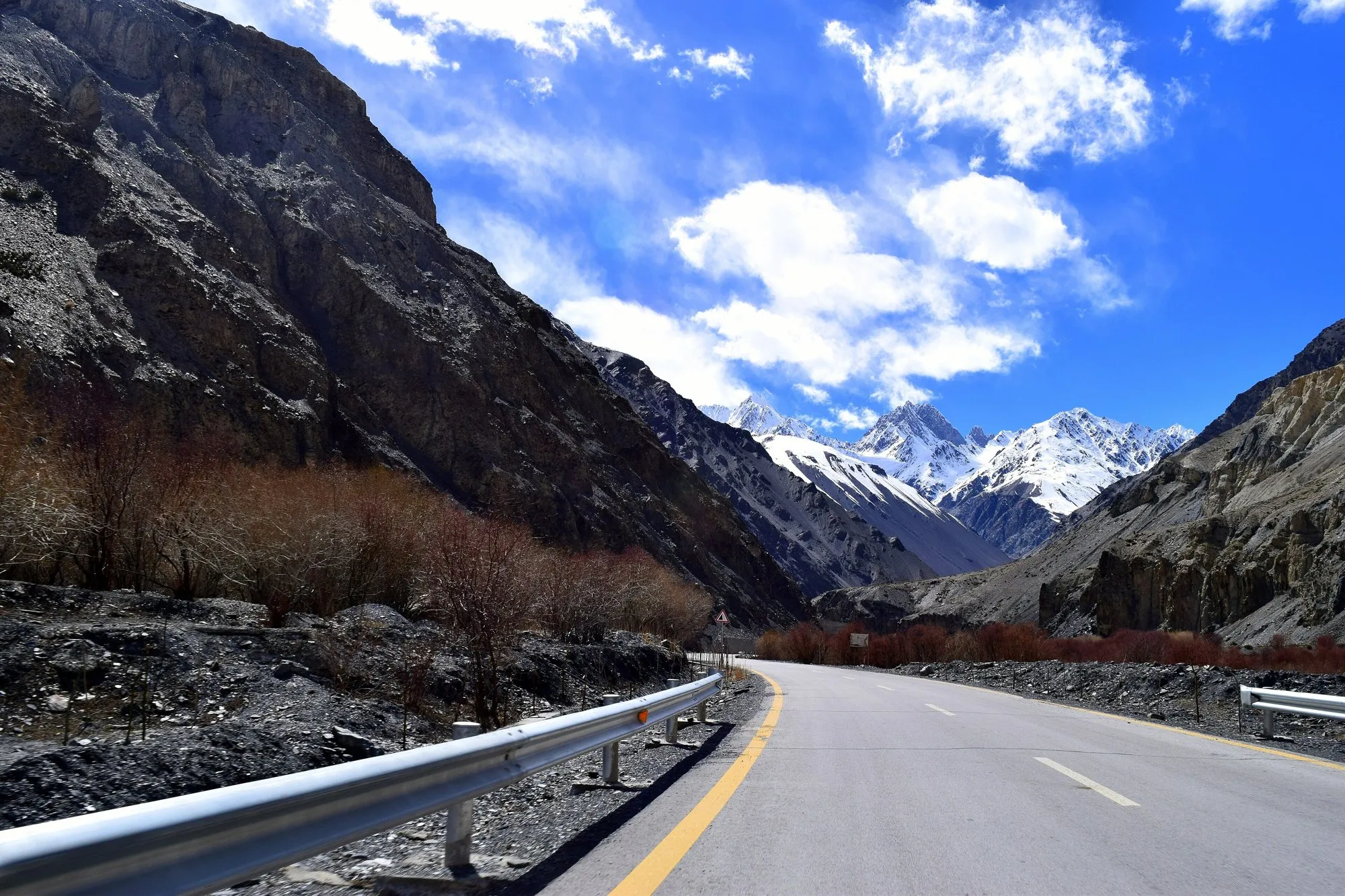 The paved Karakoram Highway winding up a rocky valley towards snowy peaks in Hunza