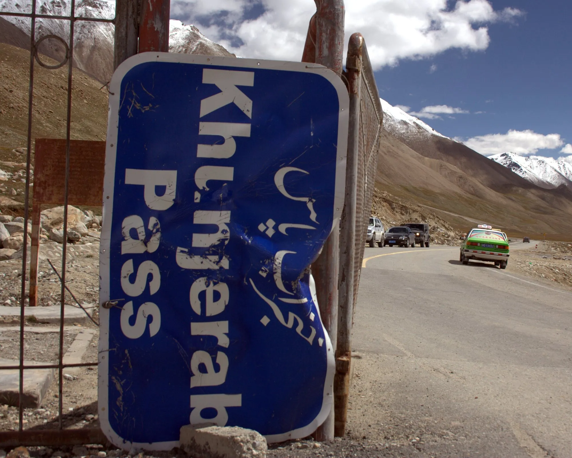 A battered blue Khunjerab Pass sign beside the road near the border