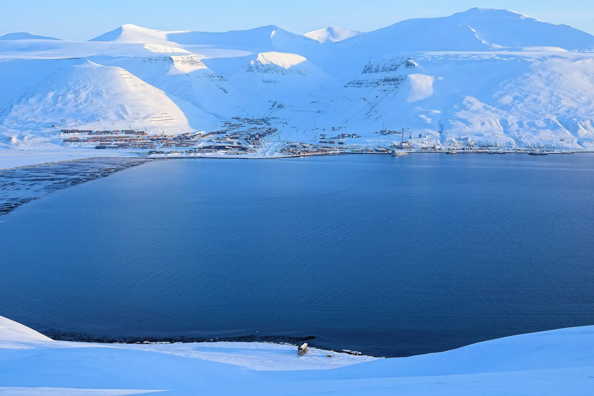 Longyearbyen spread along a fjord shore under snow-covered mountains, seen from above