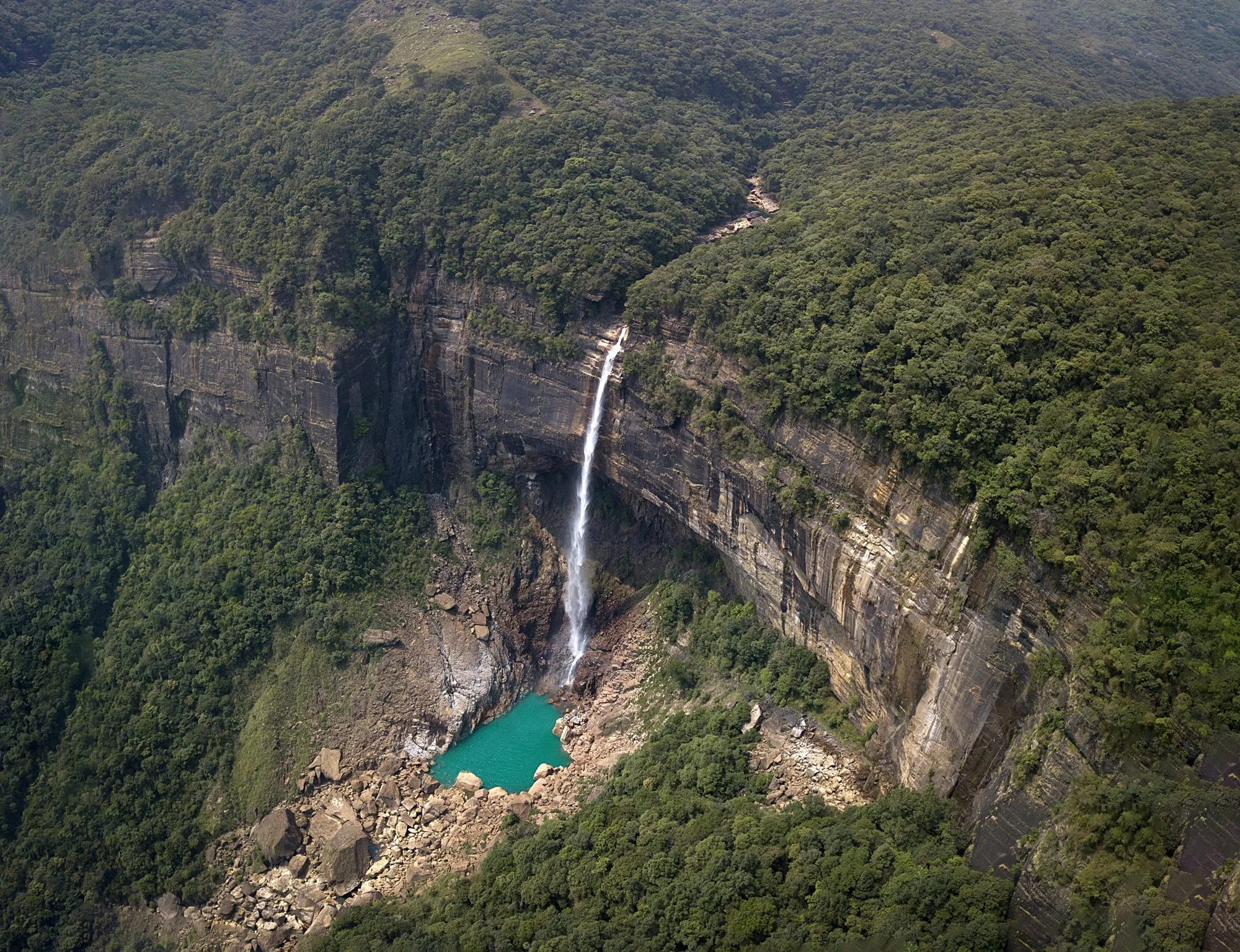 Nohkalikai Falls plunging down a sheer cliff into a turquoise pool in a forested gorge