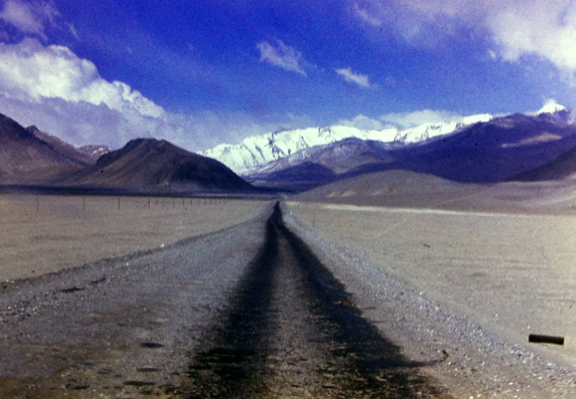 An empty gravel road across a high, bare plateau towards snowy mountains