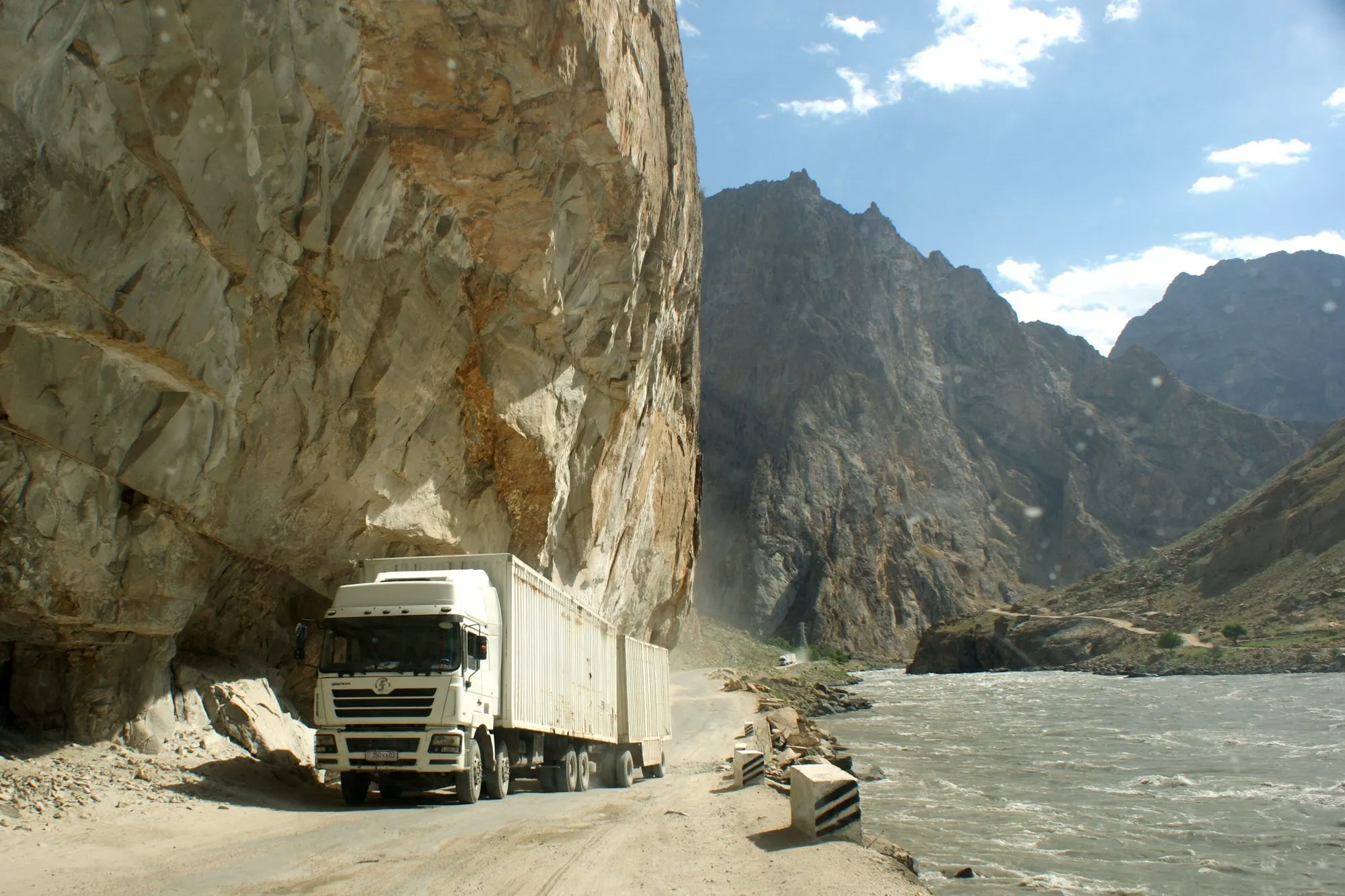 A lorry on a narrow road cut into a cliff above the Panj River