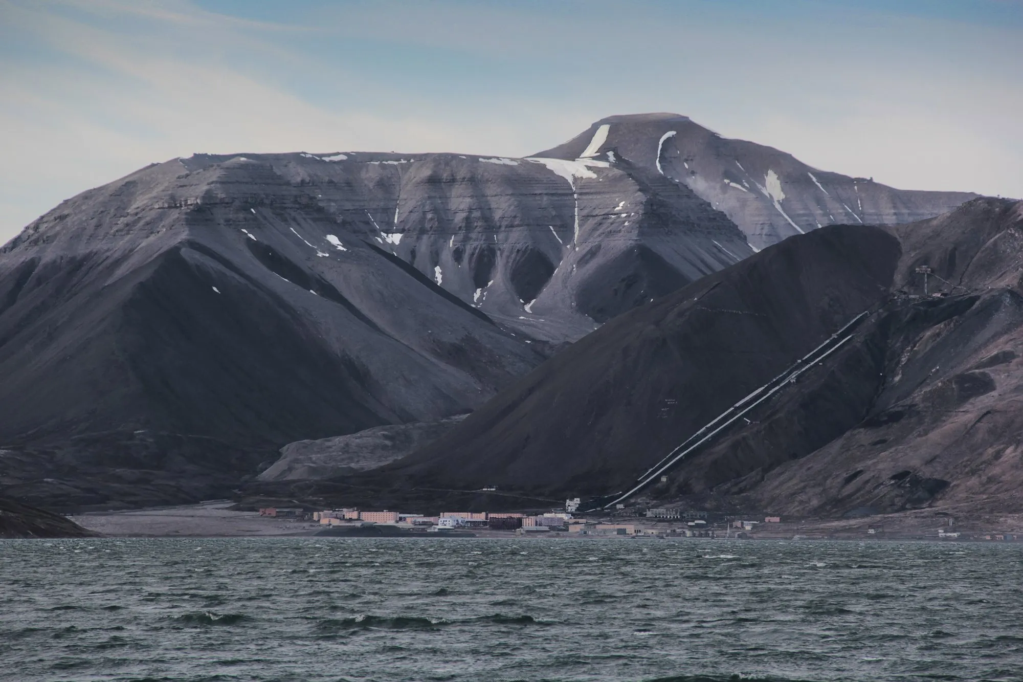 The abandoned settlement of Pyramiden at the foot of a pyramid-shaped mountain, seen from a boat