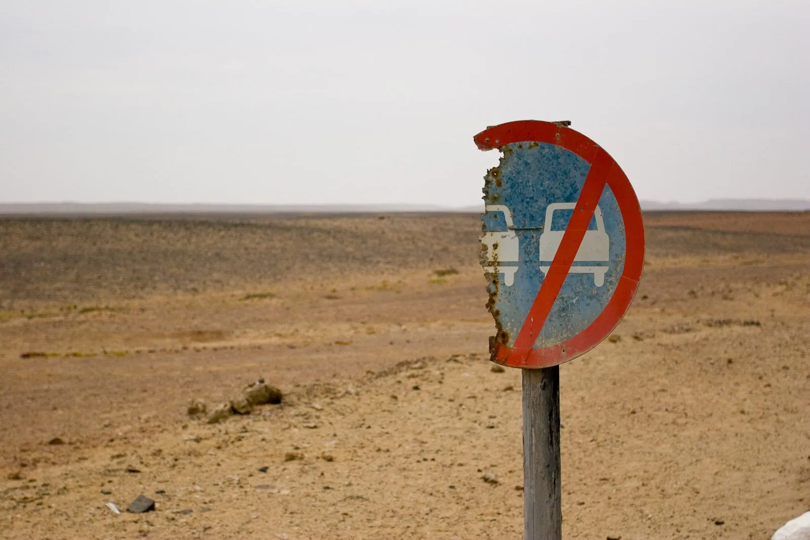 A rusty, sand-blasted road sign on a flat gravel plain