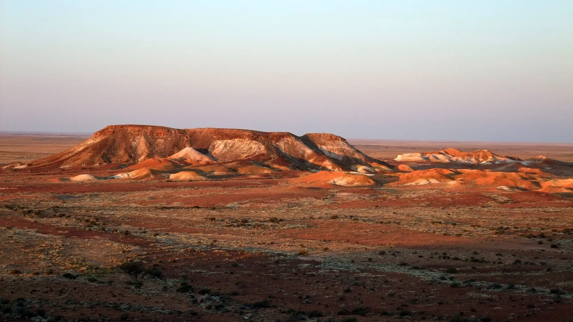 Flat-topped mesas of the Breakaways glowing orange at sunset near Coober Pedy