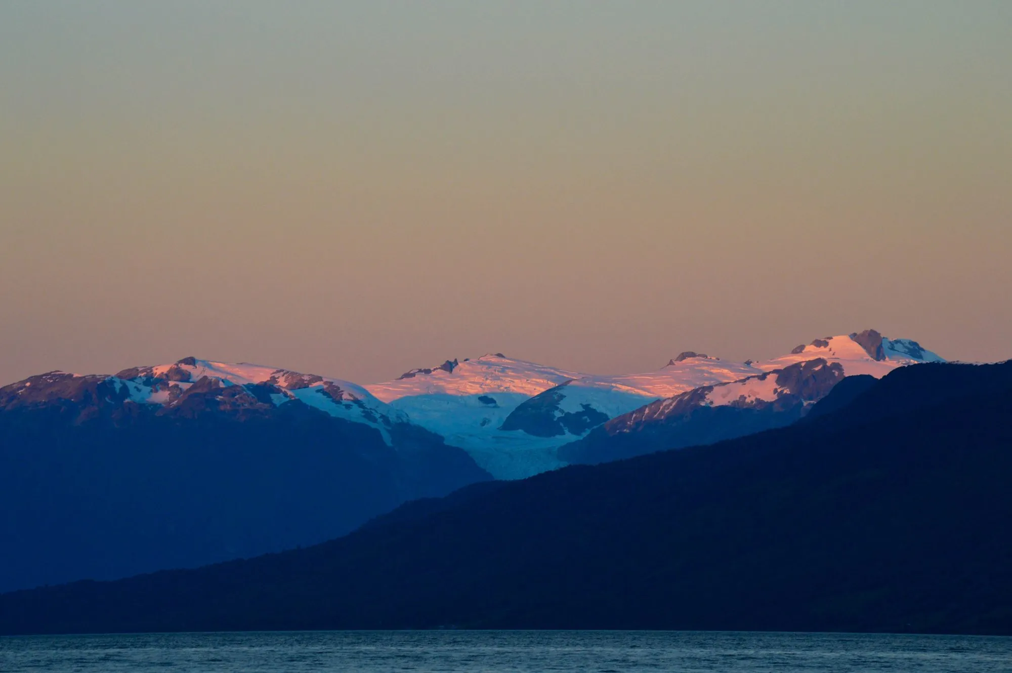 Pink sunset light on glaciated peaks above a dark fjord in Queulat National Park