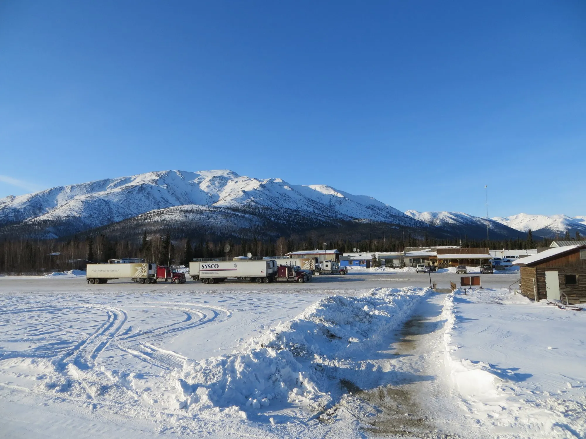 Lorries parked at the Coldfoot truck stop in snow, with mountains behind